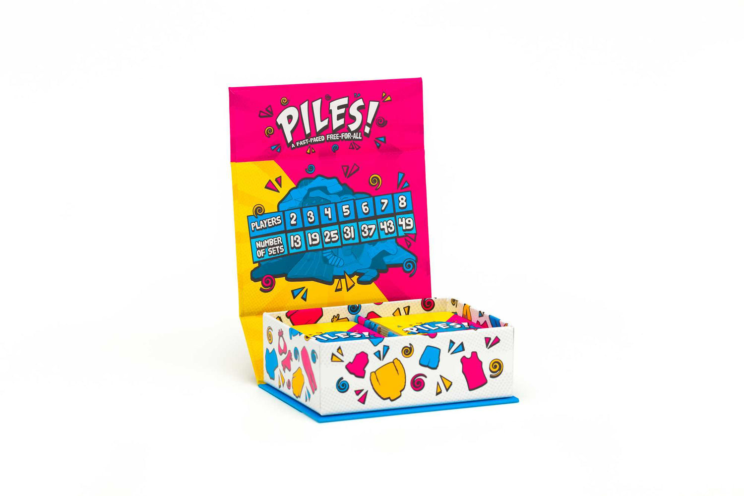 Eine Spielbox mit dem Titel 'Piles!' ist geöffnet und zeigt Spieldetails. Die Box ist mit bunten Formen und Text auf weißem Hintergrund verziert.