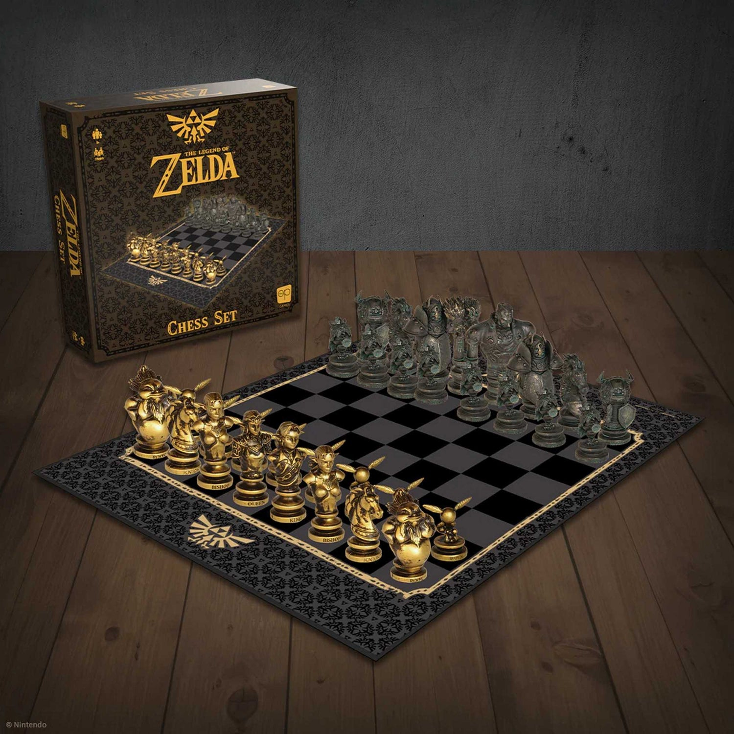 Un set di scacchi di Zelda. Pezzi dorati e trasparenti su una scacchiera nera e grigia. La scatola è sullo sfondo.