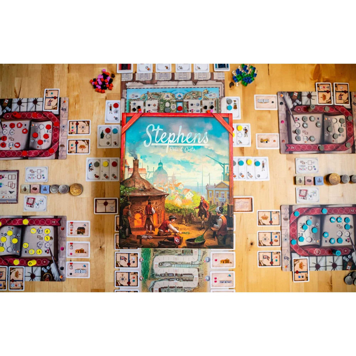 Brettspiel 'Stephens' auf einem Holztisch. Karten, Spielsteine und Spielteile umgeben die Schachtel mit Kunst von Menschen in der Nähe eines Ofens.