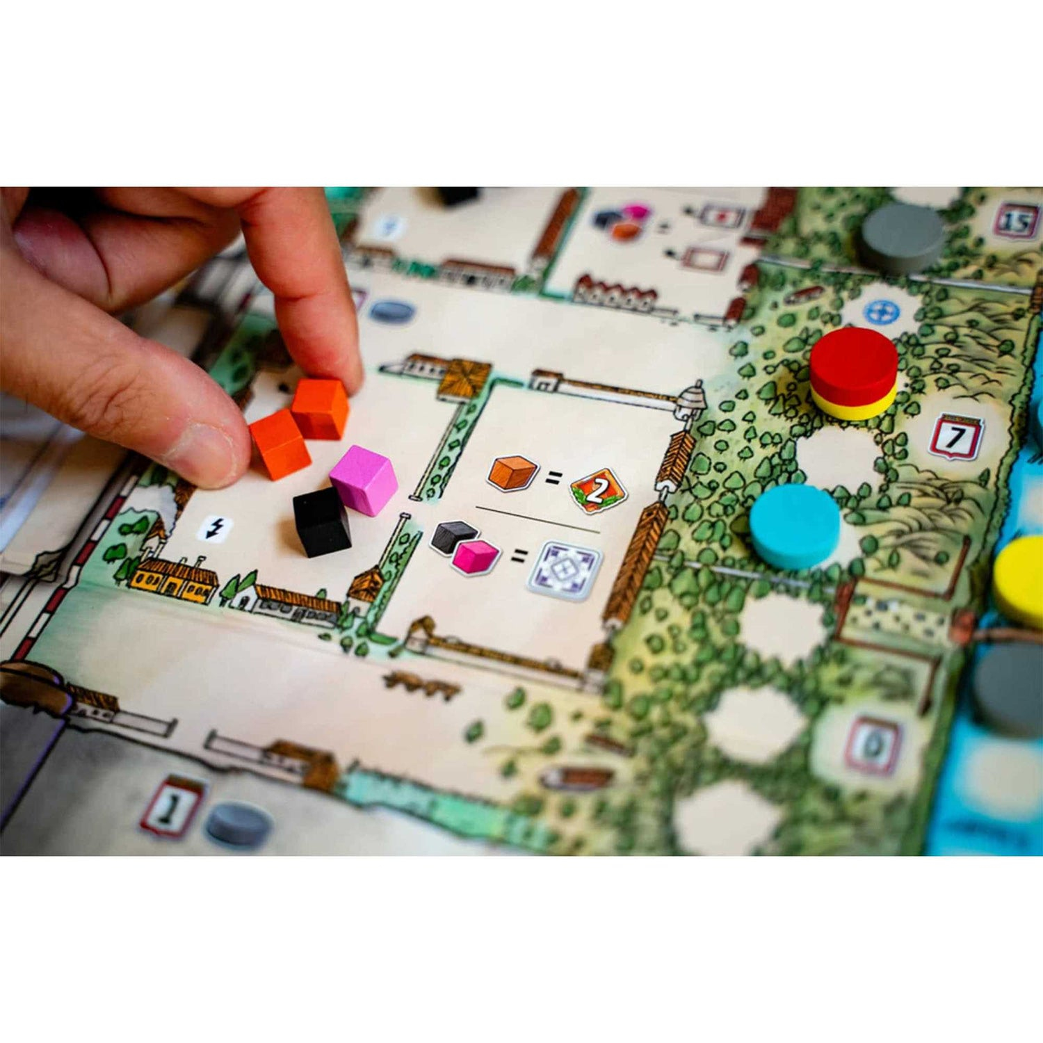Eine Hand platziert farbige Würfel auf einem Brettspiel. Das Brett zeigt eine Karte mit Gebäuden und Markierungen. Andere Spielsteine sind vorhanden.