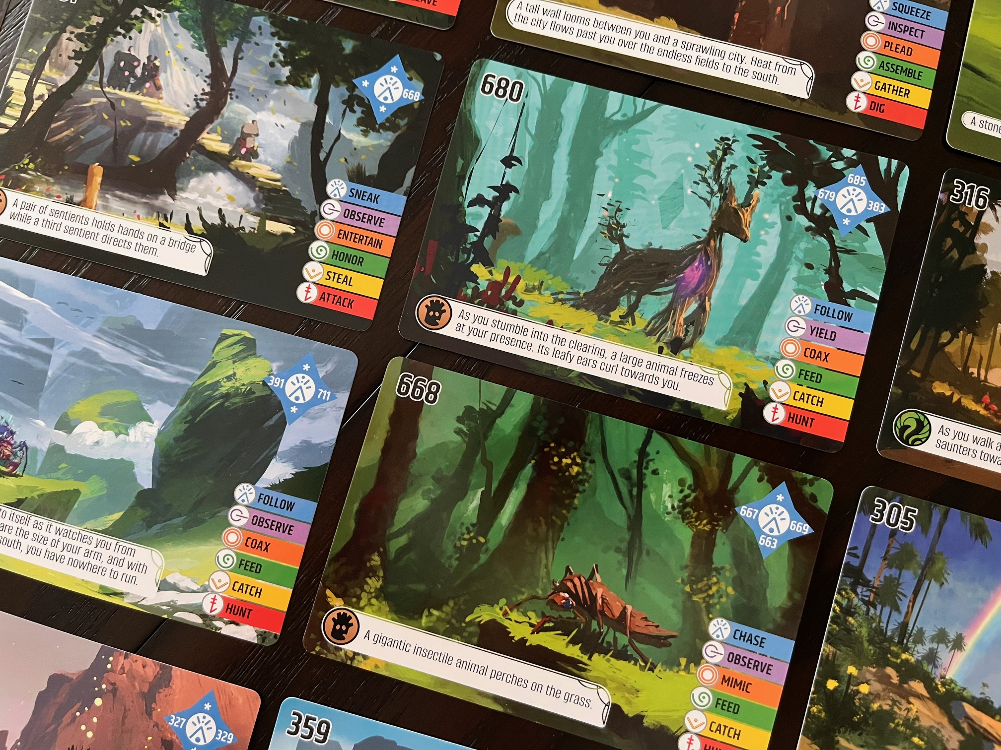 Kaarten van een bordspel liggen op een houten tafel. De kaarten tonen verschillende illustraties en spelmechanismen.