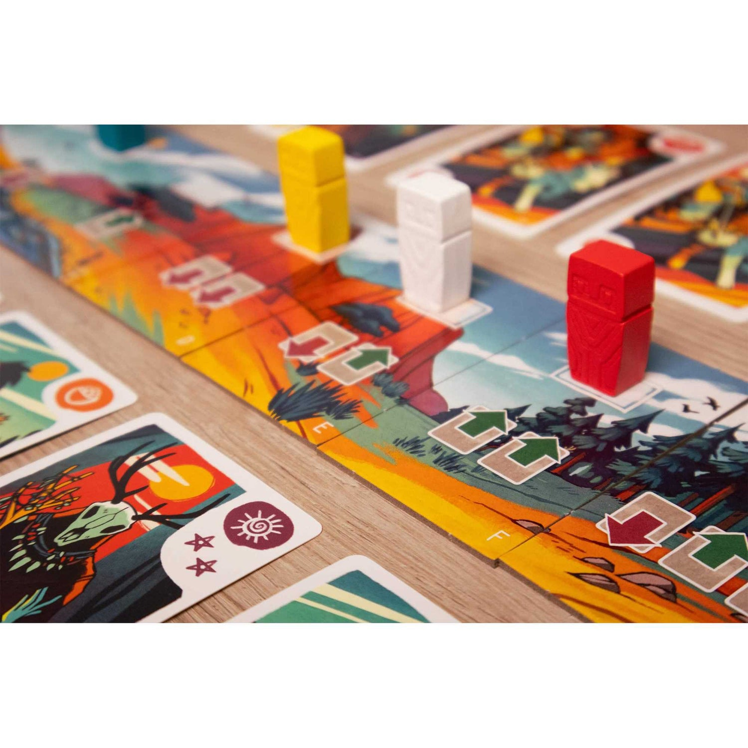 Brettspiel-Setup. Holzbrett mit farbenfroher Landschaft. Rote, gelbe und weiße Spielfiguren. Karten mit Illustrationen sind platziert.
