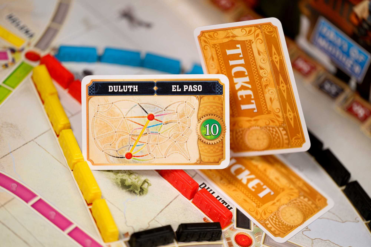 Ein Brettspiel mit Karten, die Routen zwischen Duluth und El Paso zeigen. Gelbe, rote und blaue Zugteile sind sichtbar.