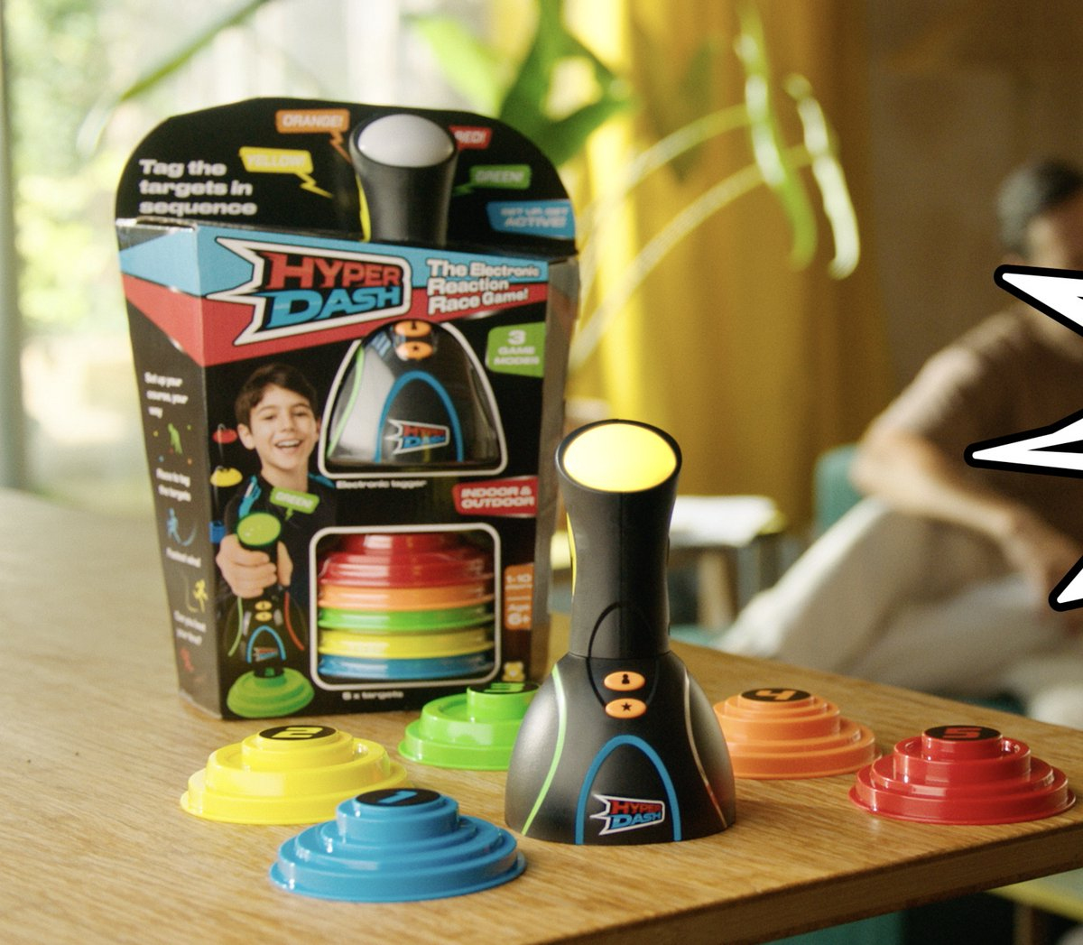 Een speldoos met een jongen, een zwart spelapparaat en kleurrijke doelen op een houten tafel. Een wazige persoon op de achtergrond.