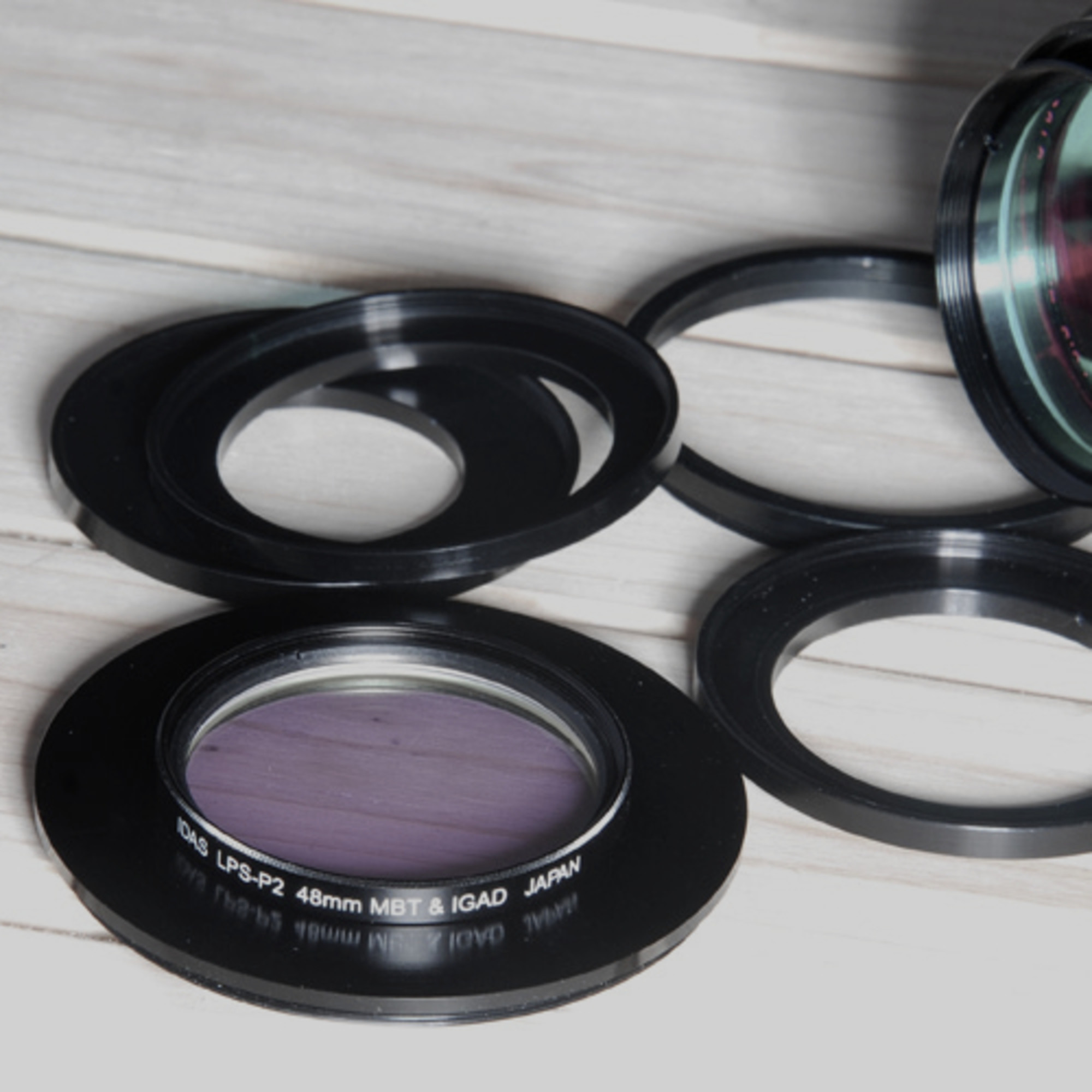 Mehrere schwarze Kameraobjektivfilter und -ringe liegen auf einer hellen Holzoberfläche. Ein Filter hat violettes Glas.