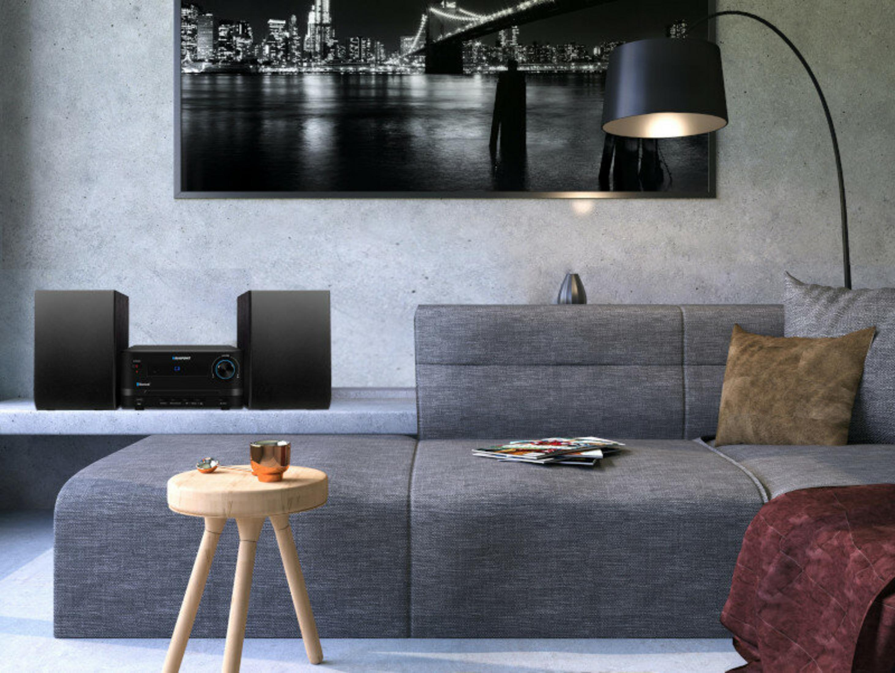 Scena w salonie z sofą, lampą, zestawem stereo i obrazem miasta. Kubek i czasopisma na stole.