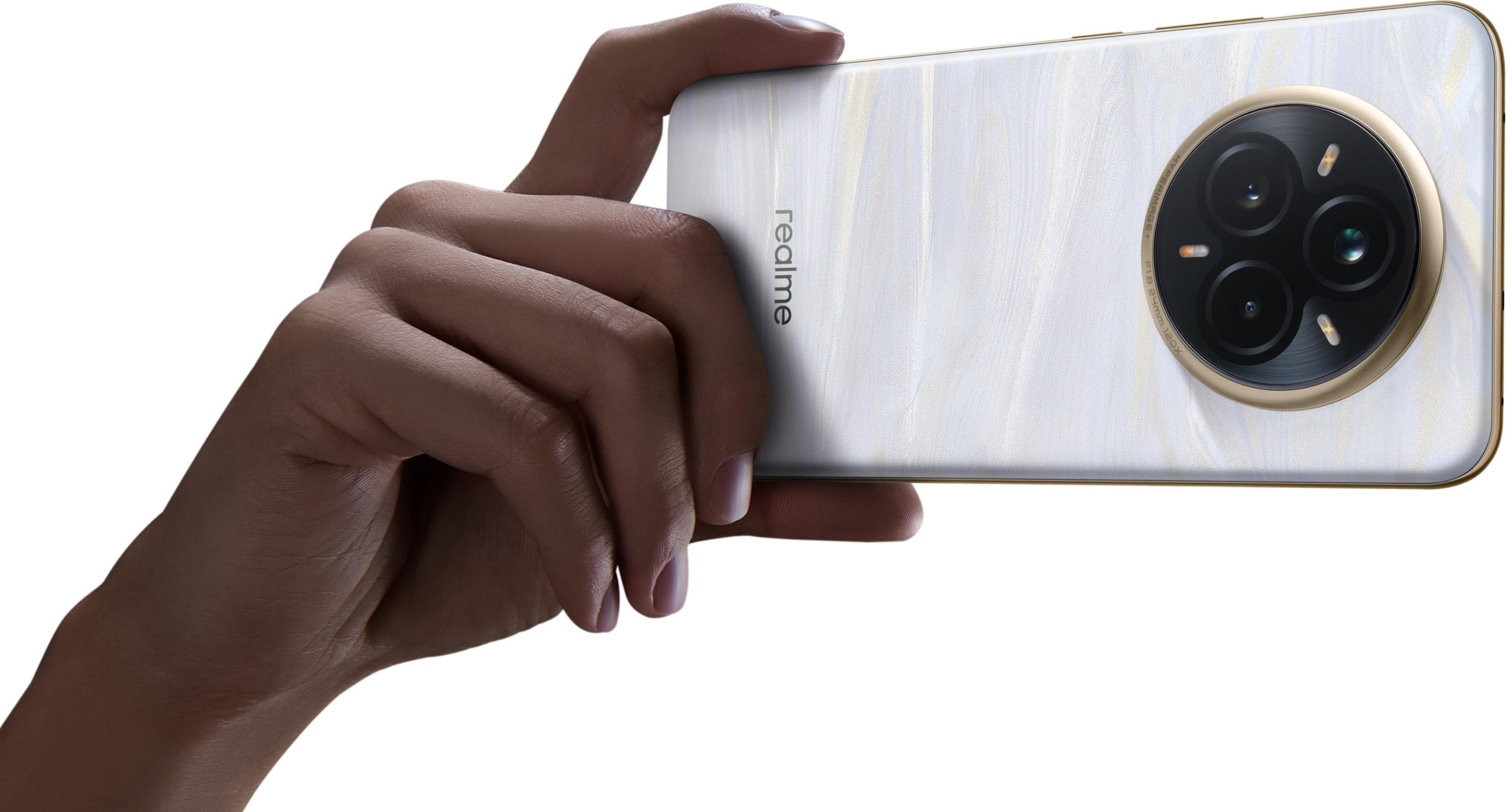 Dłoń trzyma biały smartfon ze złotymi akcentami. Telefon ma potrójny obiektyw aparatu, widoczne logo Realme.