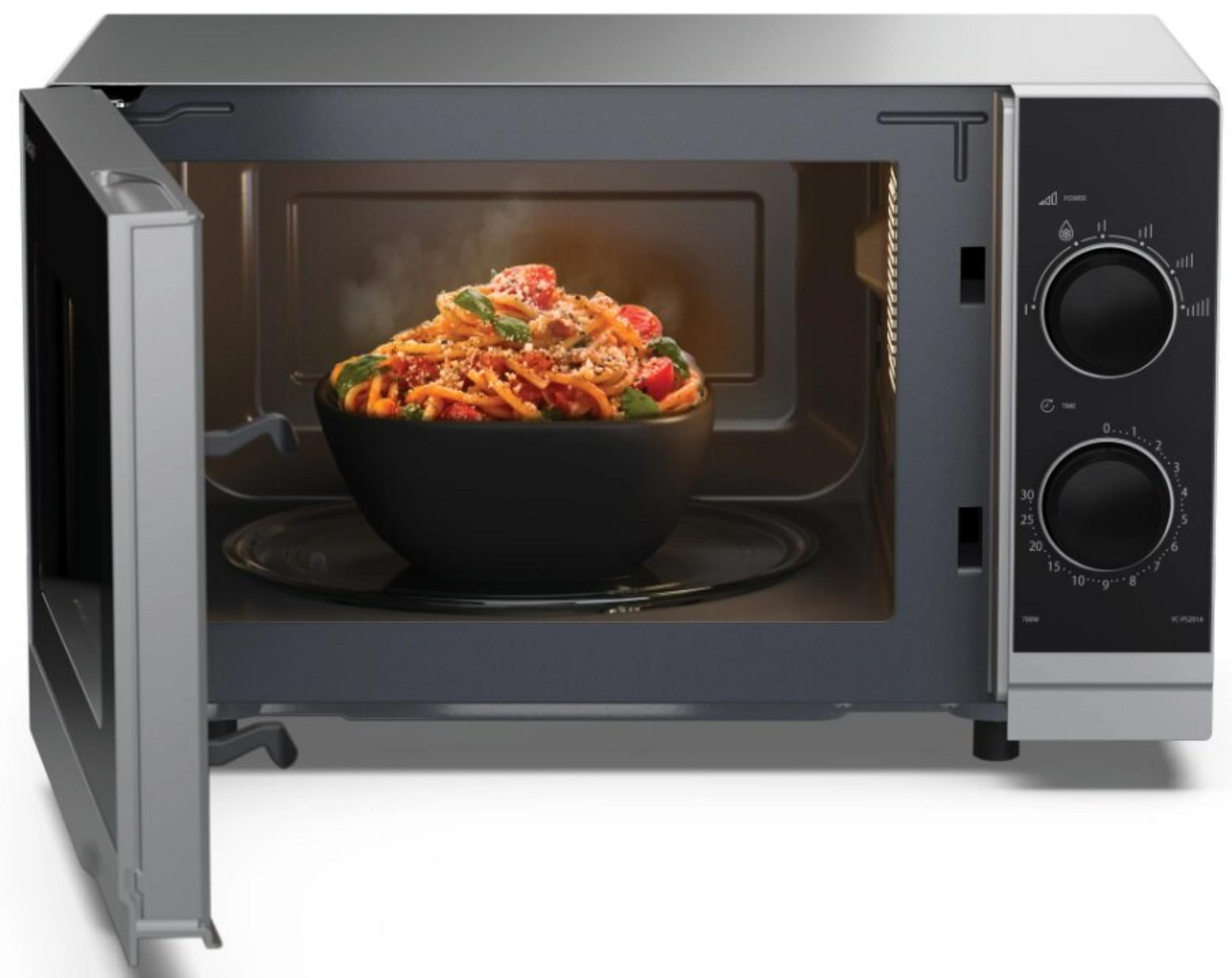 Un microondas con la puerta abierta. Dentro, se ve un plato de pasta con tomates y albahaca. El microondas es plateado y negro.