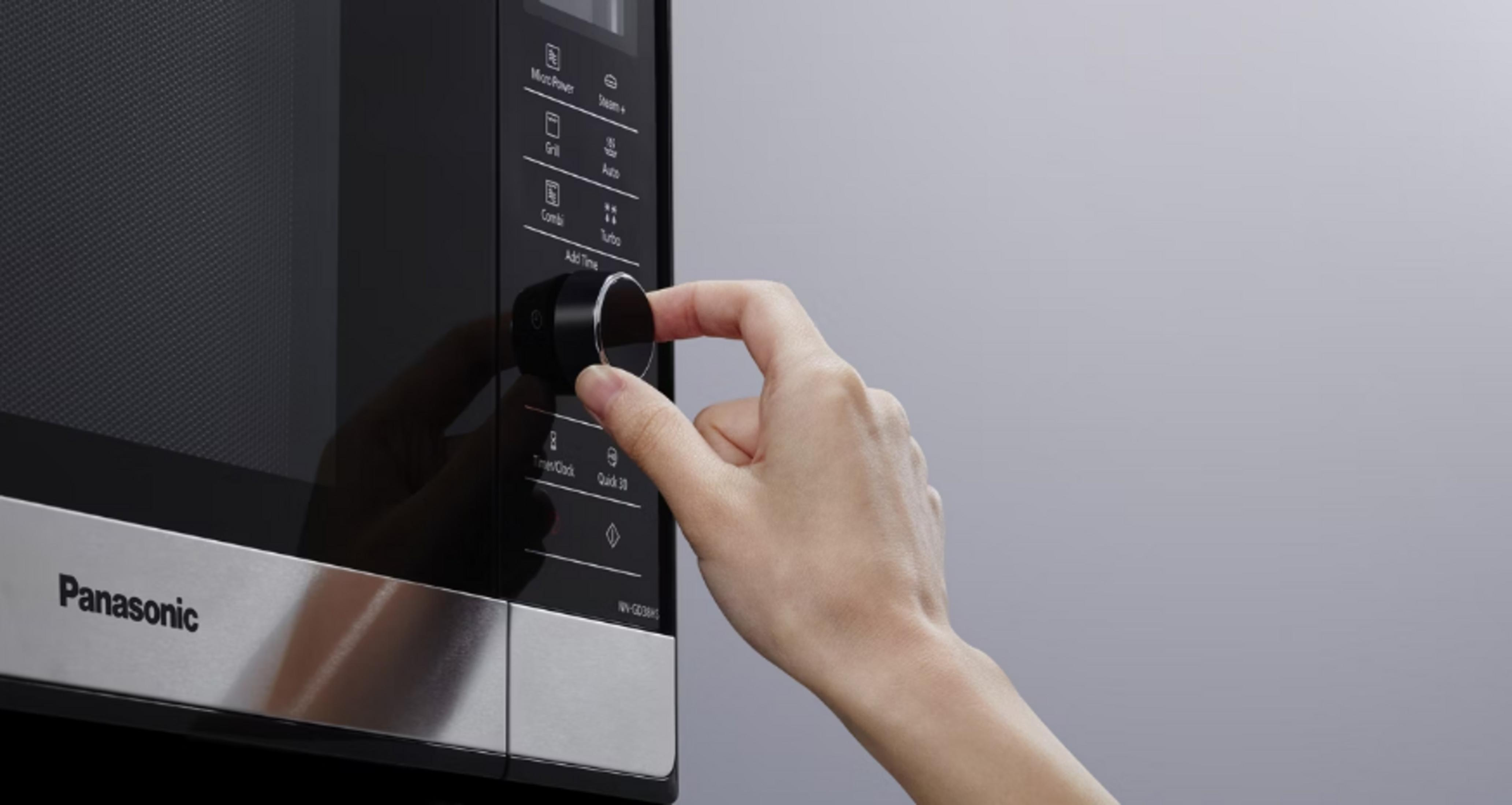 Ręka obraca pokrętło czarnej kuchenki mikrofalowej Panasonic. Pokrętło jest ostre, widoczny panel sterowania.