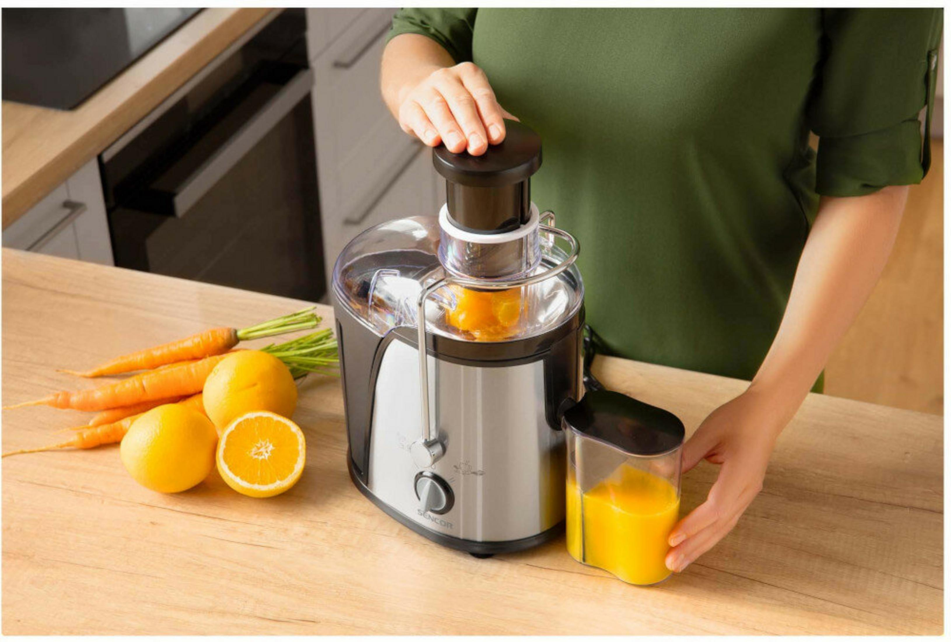 Una persona usa un'estrattore. Arance, carote e succo sono visibili.