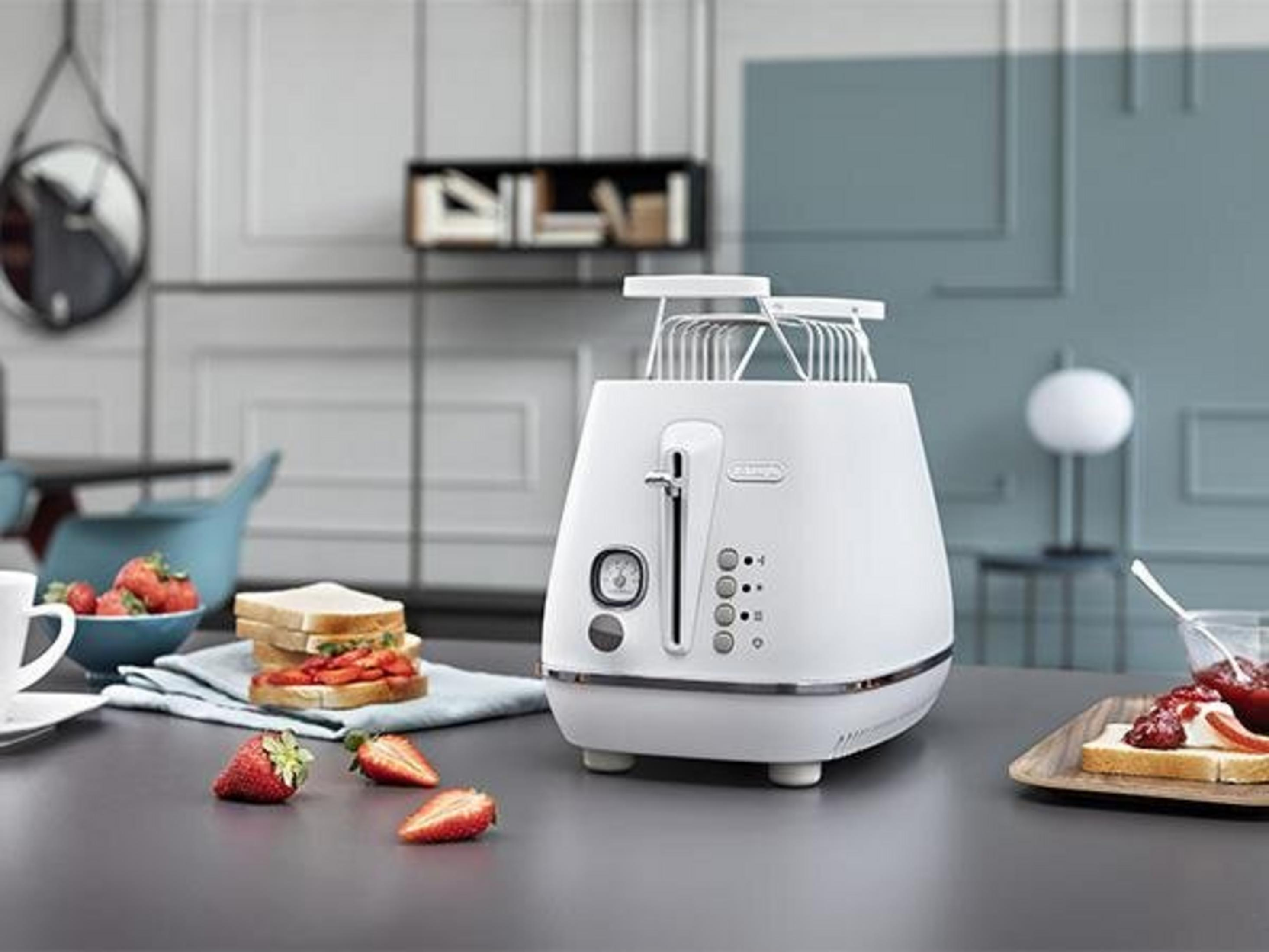 Weißer Toaster, Brot, Erdbeeren, Sandwich und Marmelade auf einem Tisch. Eine Schale mit Erdbeeren und ein Spiegel im Hintergrund.