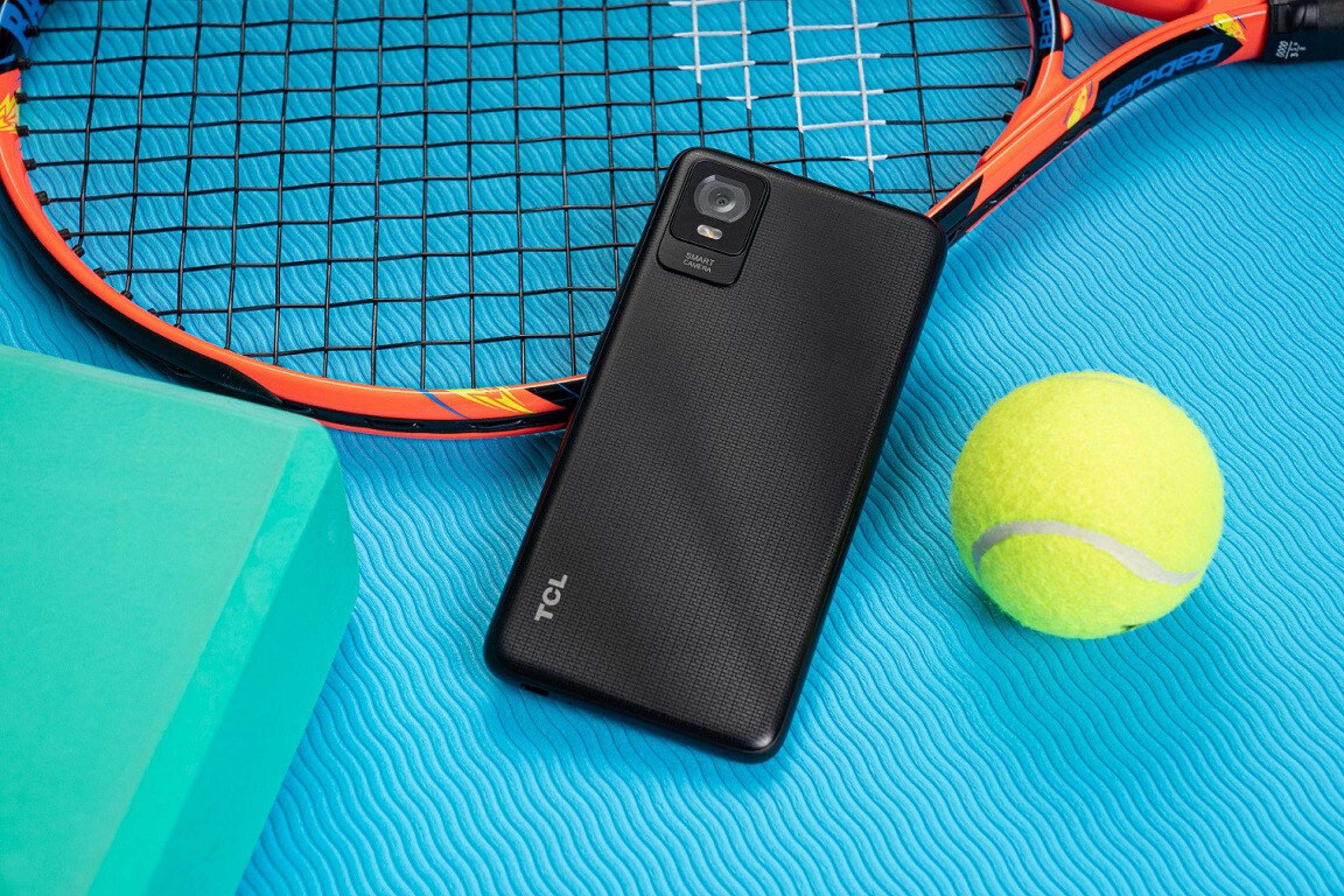 Un smartphone negro, una raqueta de tenis, una pelota de tenis y un bloque verde sobre una superficie azul.