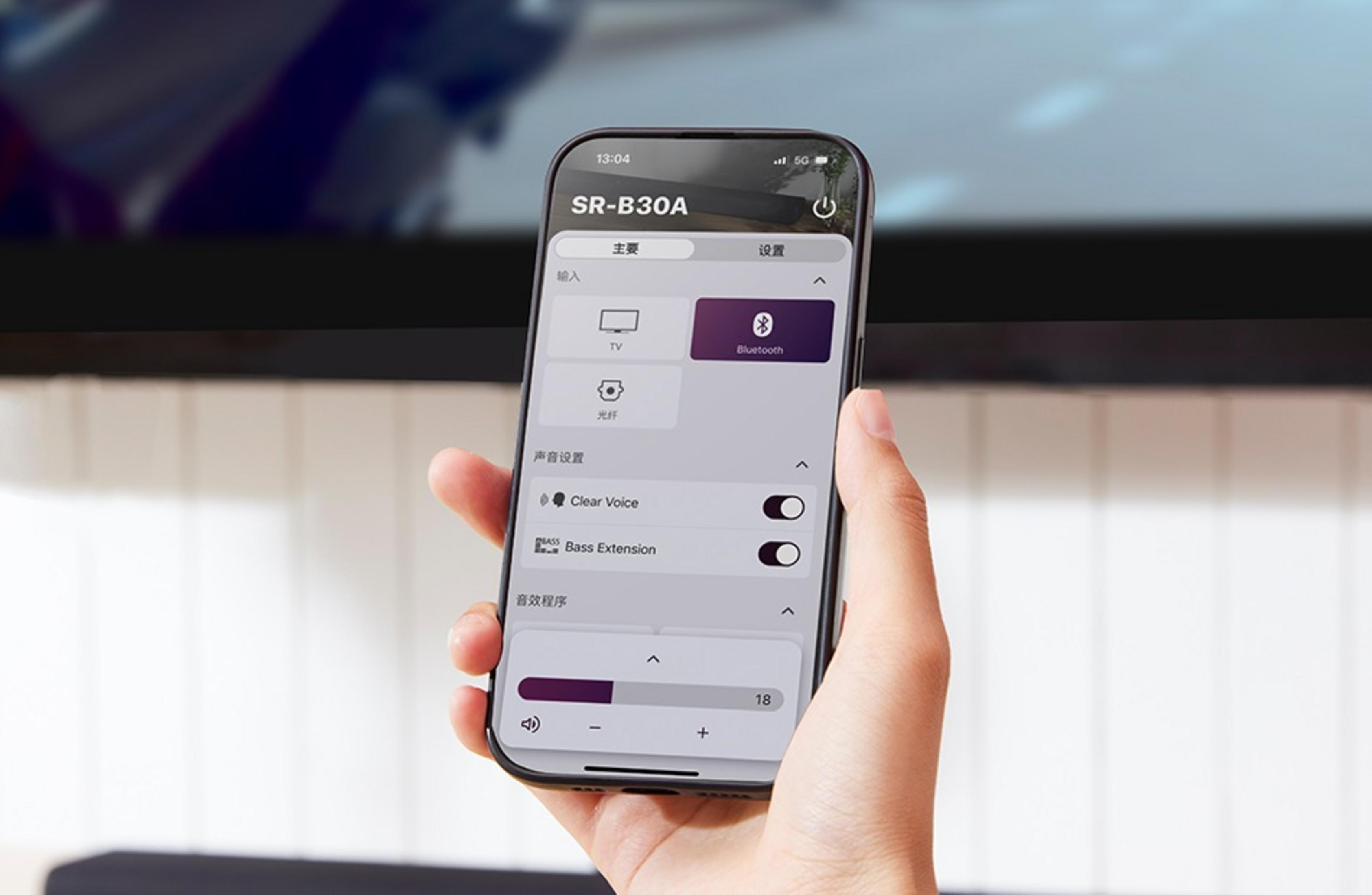 Una mano tiene uno smartphone che mostra l'interfaccia SR-B30A. Le opzioni includono TV, Bluetooth e impostazioni audio.