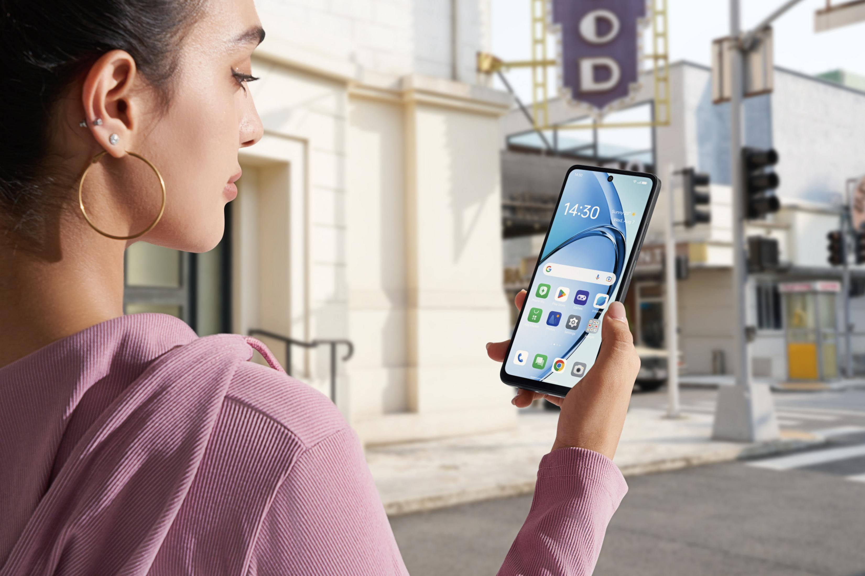 Una mujer sostiene un smartphone con la hora 14:30. Lleva una sudadera rosa y un pendiente de aro dorado.