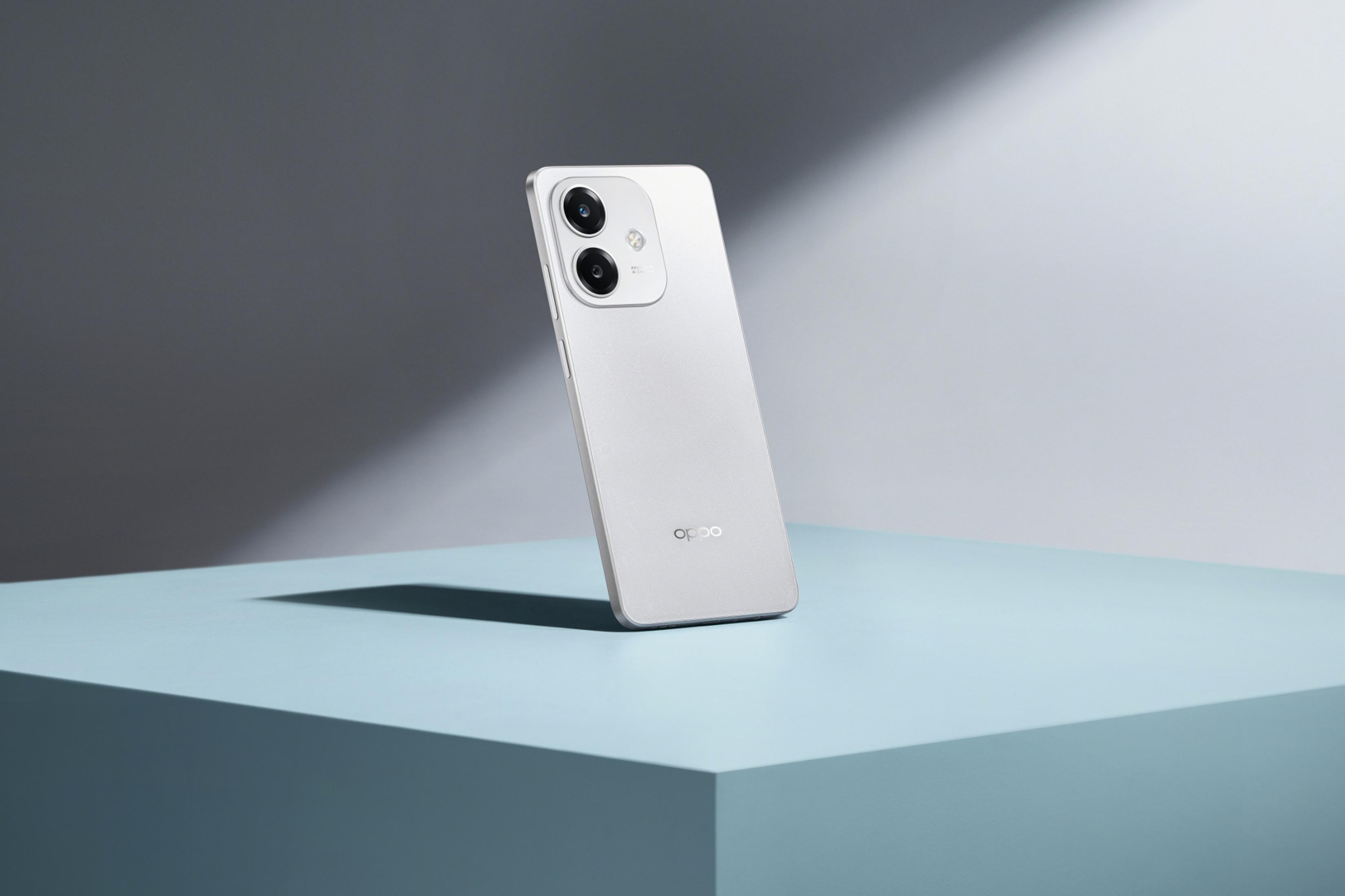 Smartphone plateado sobre una superficie azul. El fondo es un degradado gris y blanco. El teléfono está en ángulo.