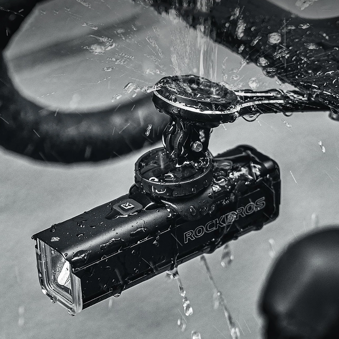 Nahaufnahme eines schwarzen Fahrradlichts mit ROCKBROS. Wassertropfen deuten auf Regen hin.