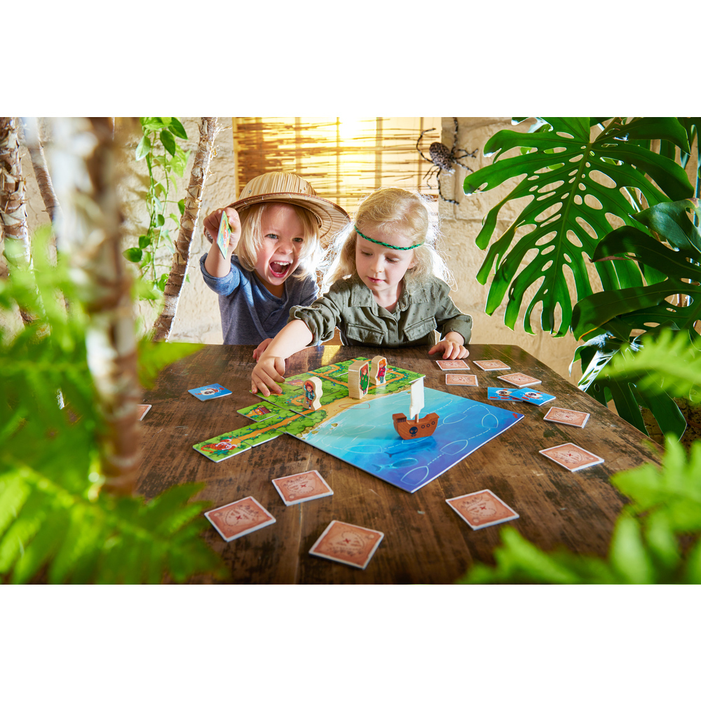 Zwei Kinder spielen ein Brettspiel mit einem Boot und Figuren. Karten und Spielbrett auf einem Holztisch. Ein Kind ist aufgeregt.