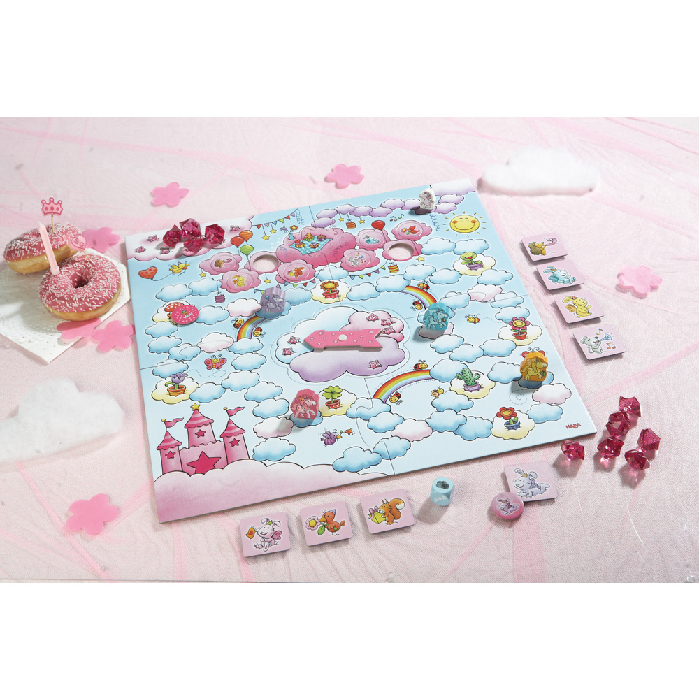 Ein Kinderspiel mit rosa Thema. Donuts, Wolken, rosa Kristalle und Spielsteine liegen auf einer rosa Tischdecke verstreut.