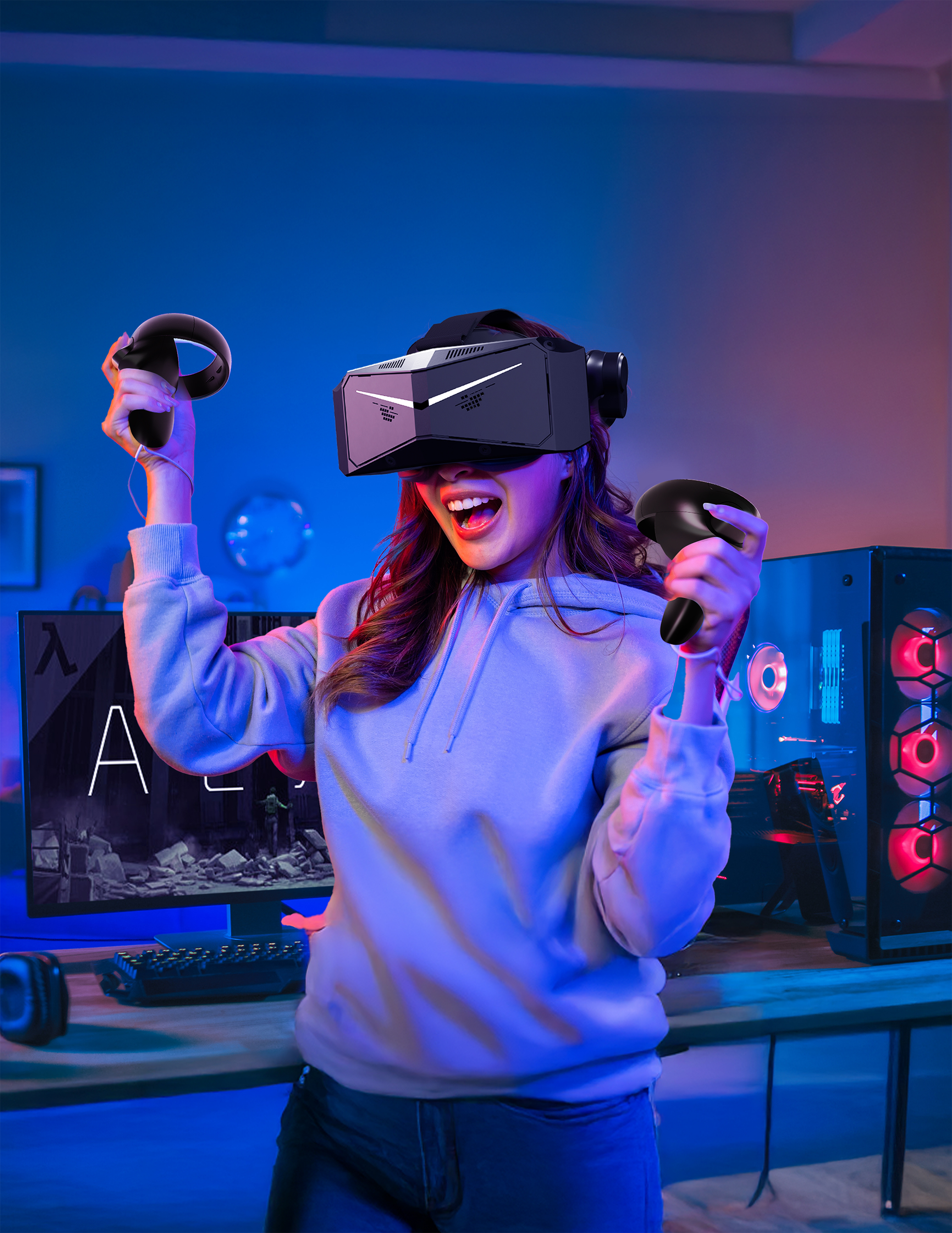 Una mujer con gafas de realidad virtual y mandos, jugando. También hay un ordenador y un monitor.