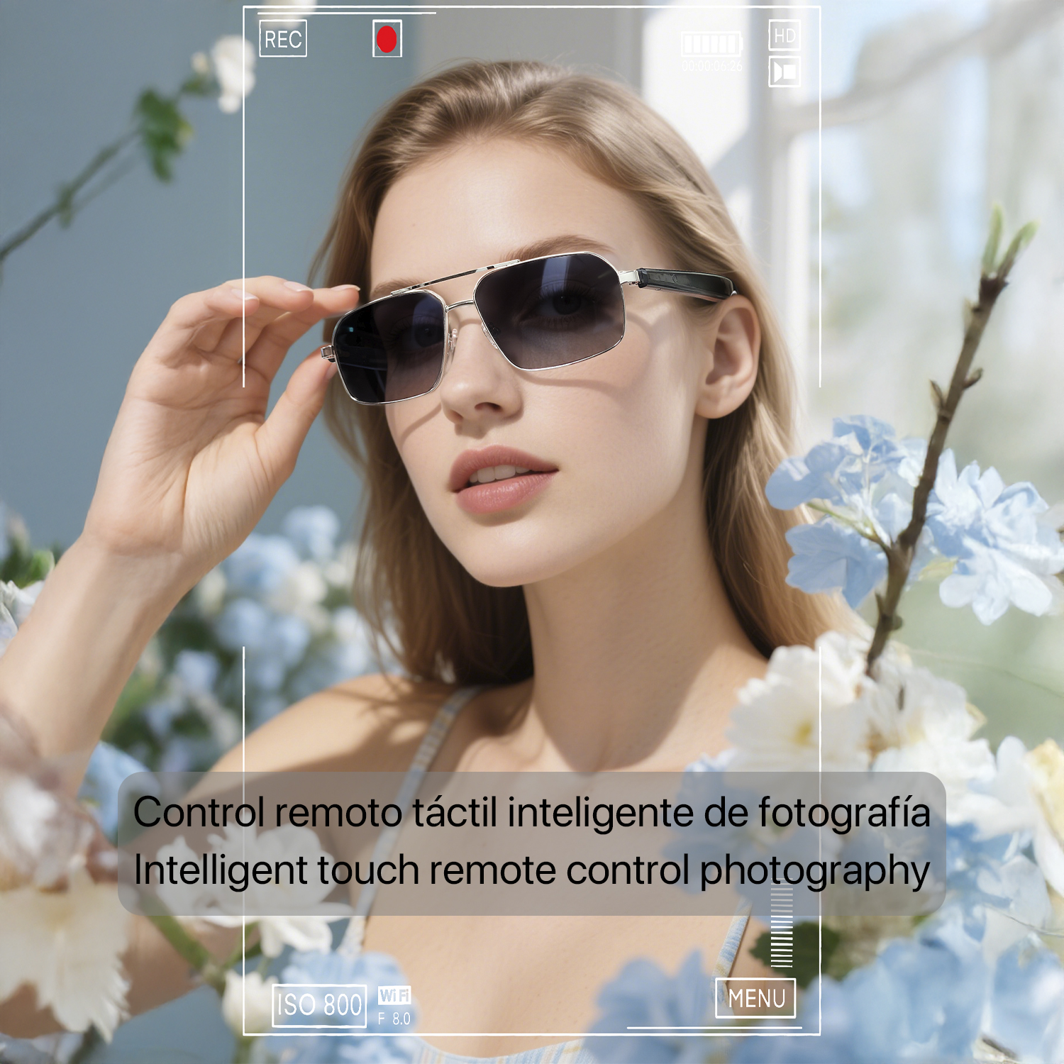 Una donna con occhiali da sole li solleva. È circondata da fiori. L'immagine ha un'interfaccia fotocamera sovrapposta.