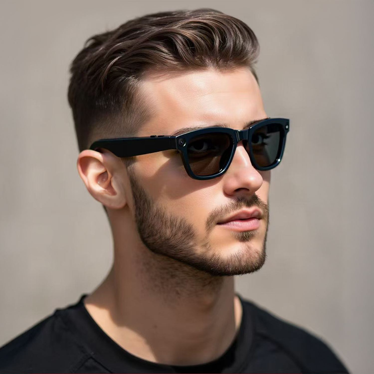 Un uomo con i capelli castani indossa occhiali da sole. Ha la barba e indossa una maglietta nera. Lo sfondo è un muro liscio.