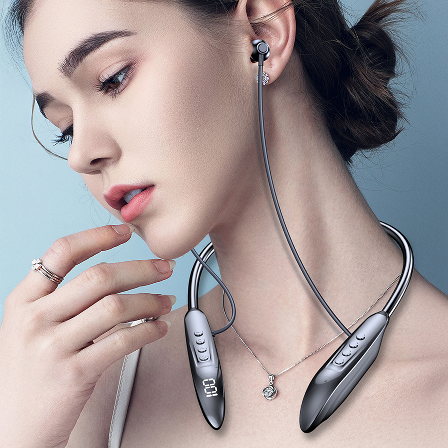 Una donna che indossa un auricolare a fascia, che guarda in basso. L'auricolare è nero e argento. Indossa anche una collana e anelli.
