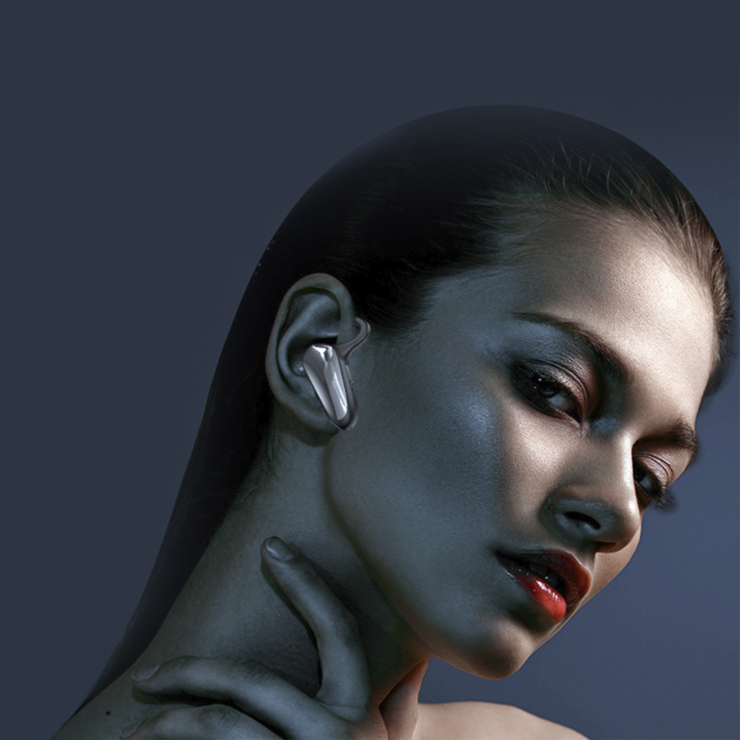 Una donna con capelli scuri e rossetto rosso indossa un auricolare argentato. Le tonalità blu e grigie creano un effetto di luce drammatico.