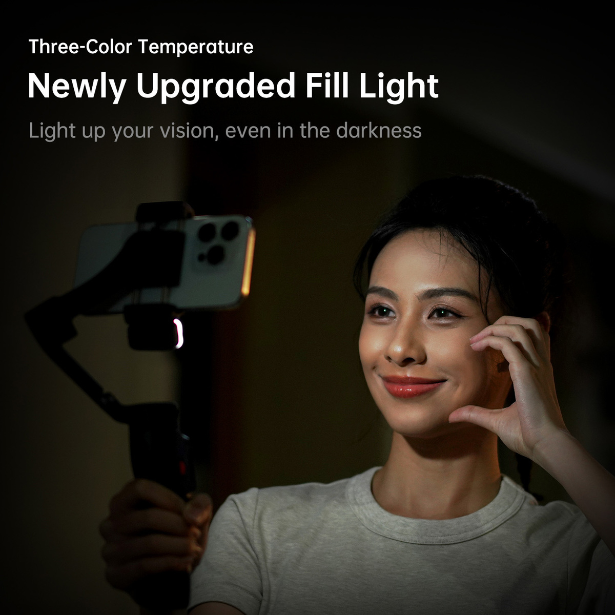 Kobieta uśmiecha się, trzymając telefon z doświetleniem. Tekst powyżej: Nowo ulepszone światło wypełniające. Tło jest ciemne.