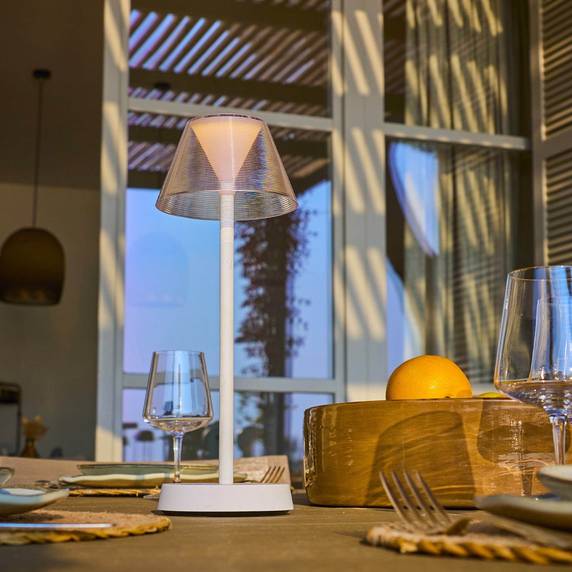 Tisch mit Lampe, Gläsern, Zitrone und Tellern. Im Hintergrund Fenster und Holzbalken.