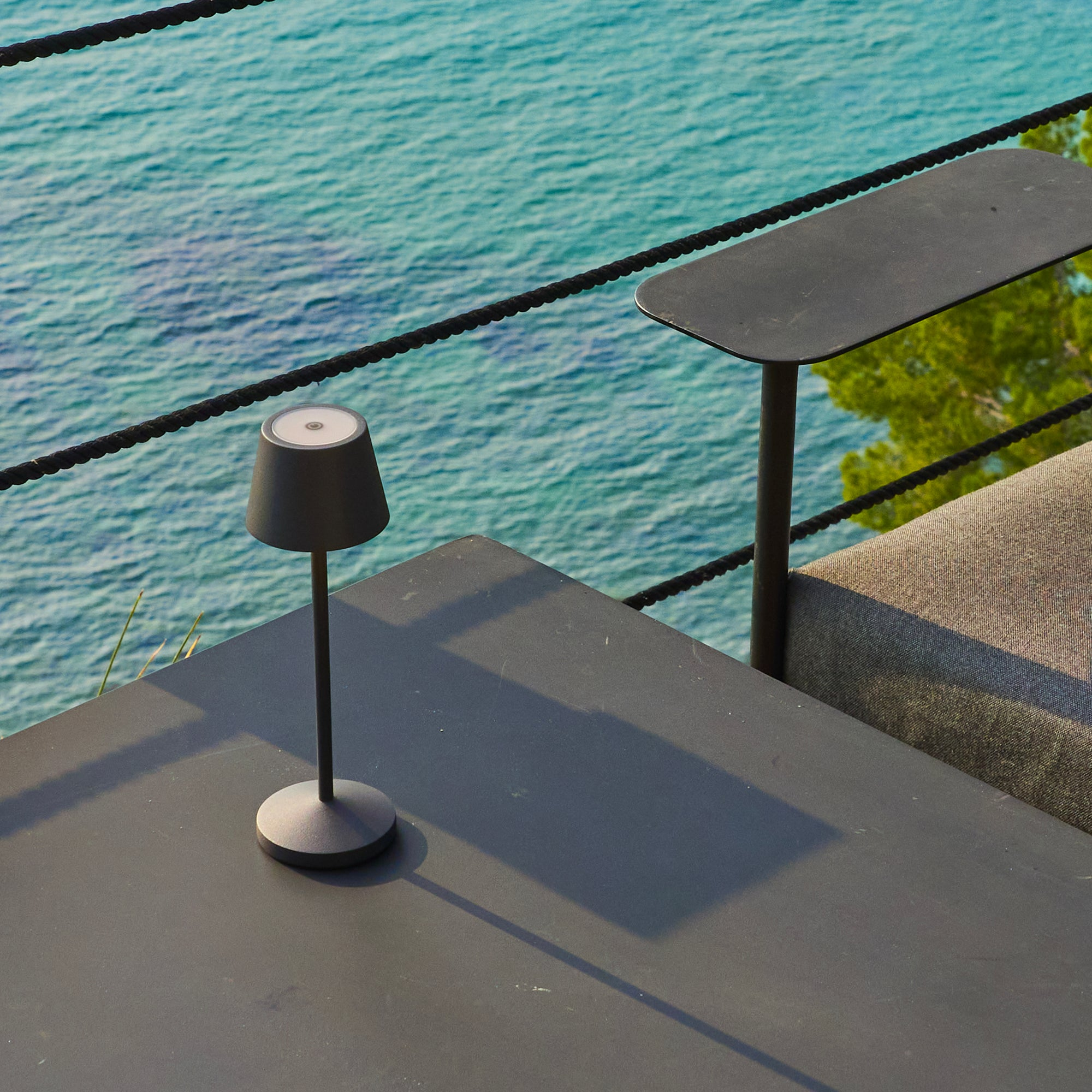 Eine dunkle Lampe auf einem Tisch, ein weiterer Tisch, schwarzes Seil und Meerblick.