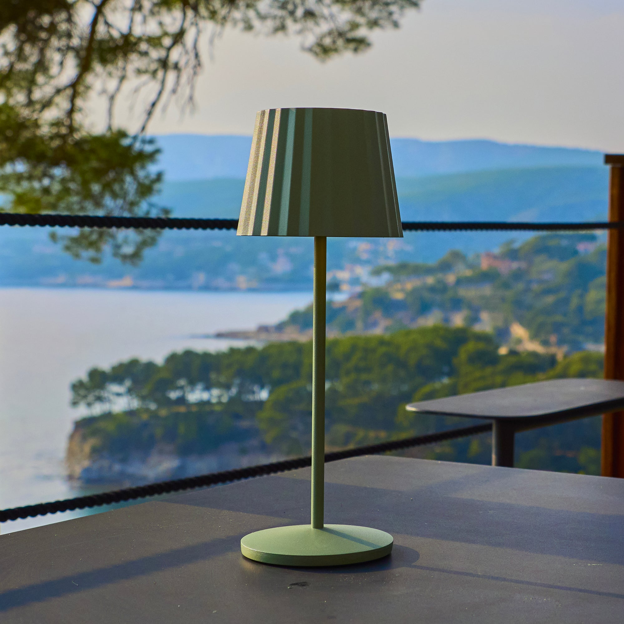 Eine grüne Lampe steht auf einem Tisch mit Blick auf das Meer und die Berge im Hintergrund.