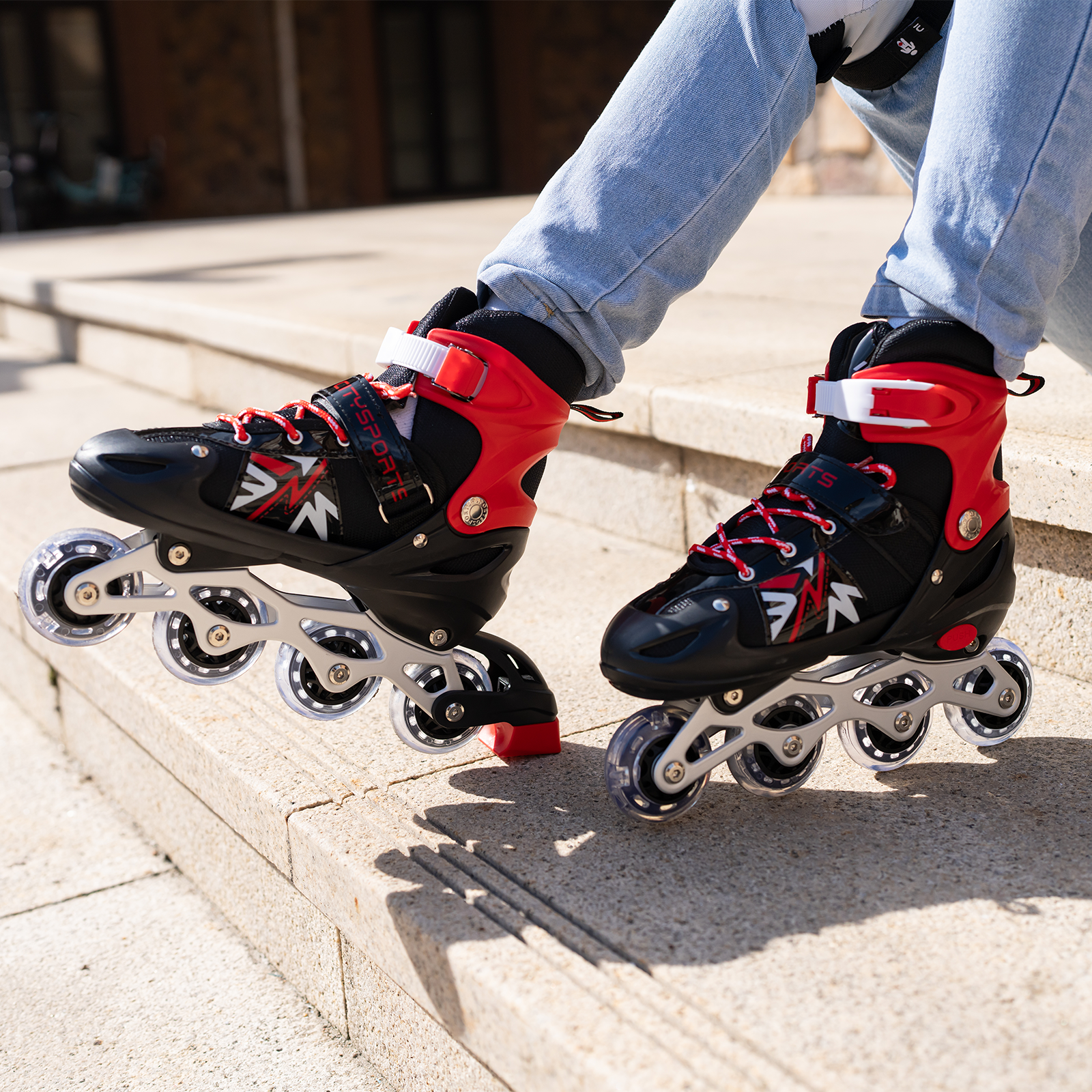 Persona con patines negros y rojos, sentada en escalones de concreto. Se ven jeans azules.