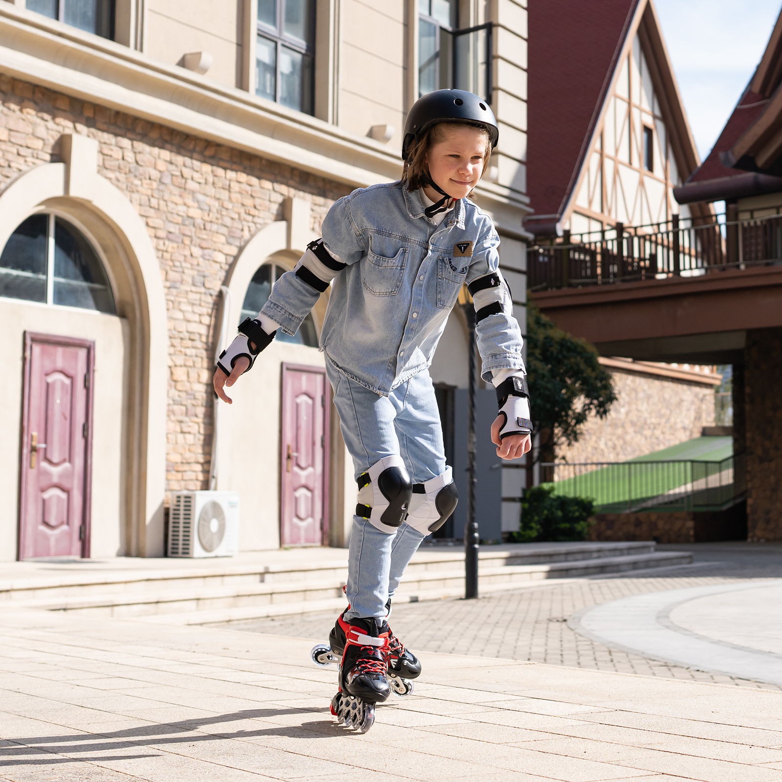 Una persona patinando sobre una superficie pavimentada. Llevan equipo de protección. Edificios al fondo.