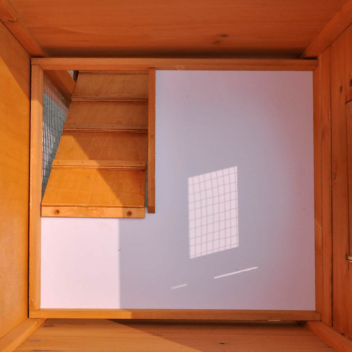 Holzstruktur mit Rampe und weißer Wand. Links befindet sich ein Metallgitter. Schatten von einem Fenster auf der Wand.