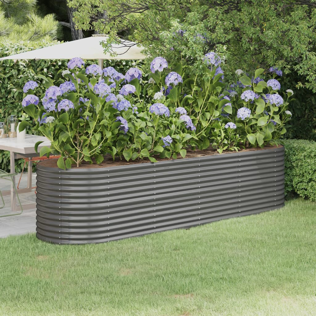 Ein Metall-Gartenbeet mit lila Hortensien gefüllt. Im Hintergrund eine Terrasse mit Tisch und Sonnenschirm, umgeben von Grün.