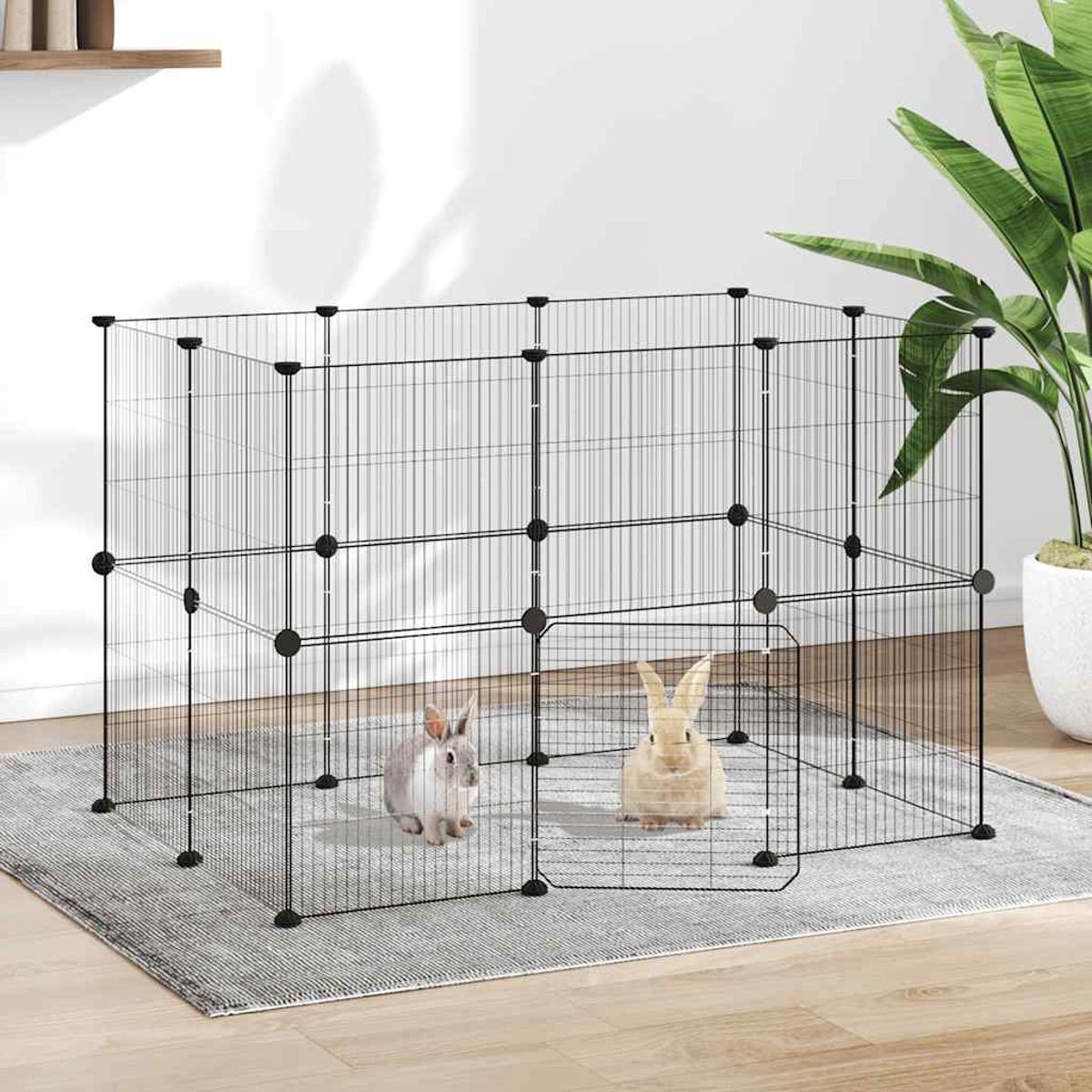 Zwei Kaninchen in einem schwarzen Drahtgehege auf einem grauen Teppich. Eine Zimmerpflanze steht im Hintergrund. Weiße Wand und Holzfußboden.