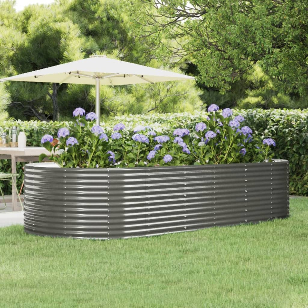 Ein erhöhtes Gartenbeet aus Metall mit lila Blumen. Ein weißer Sonnenschirm und Bäume sind im Hintergrund. Das Beet steht auf grünem Gras.