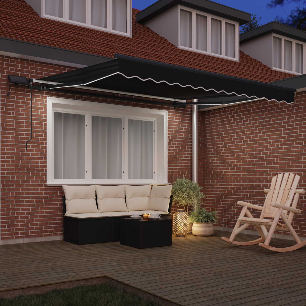 Eine Terrasse mit schwarzer Markise, Couch, Tisch und Schaukelstuhl. Rote Backsteinmauer und Haus im Hintergrund.