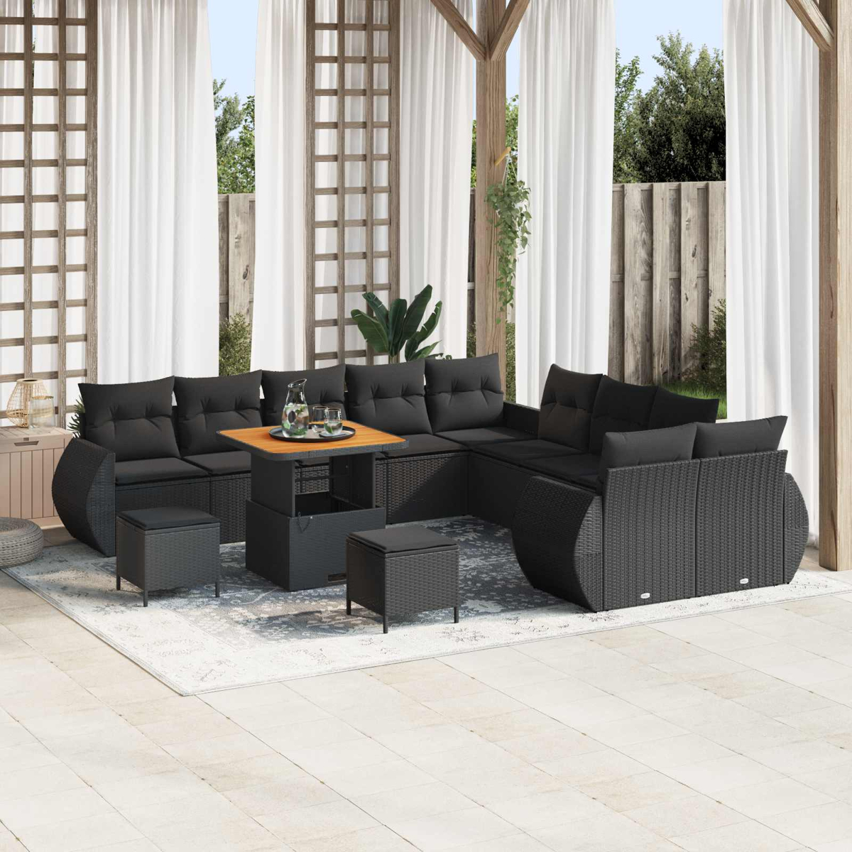 Gartensektion mit schwarzen Kissen, Tisch mit Gläsern und Krug, drei Hocker auf einem Teppich, weiße Vorhänge und Garten.