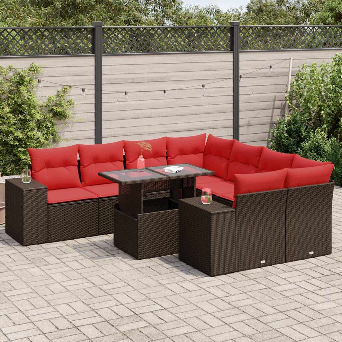 Outdoor-Ecksofa mit roten Kissen und einem Tisch mit Glasplatte auf einer Backstein-Terrasse. Im Hintergrund ein Zaun und Pflanzen.