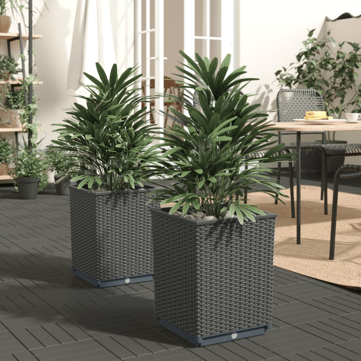 Zwei große quadratische Pflanzgefäße mit grünen Pflanzen. Terrasse mit Tisch und Stühlen im Hintergrund. Weiße Türen sind sichtbar.