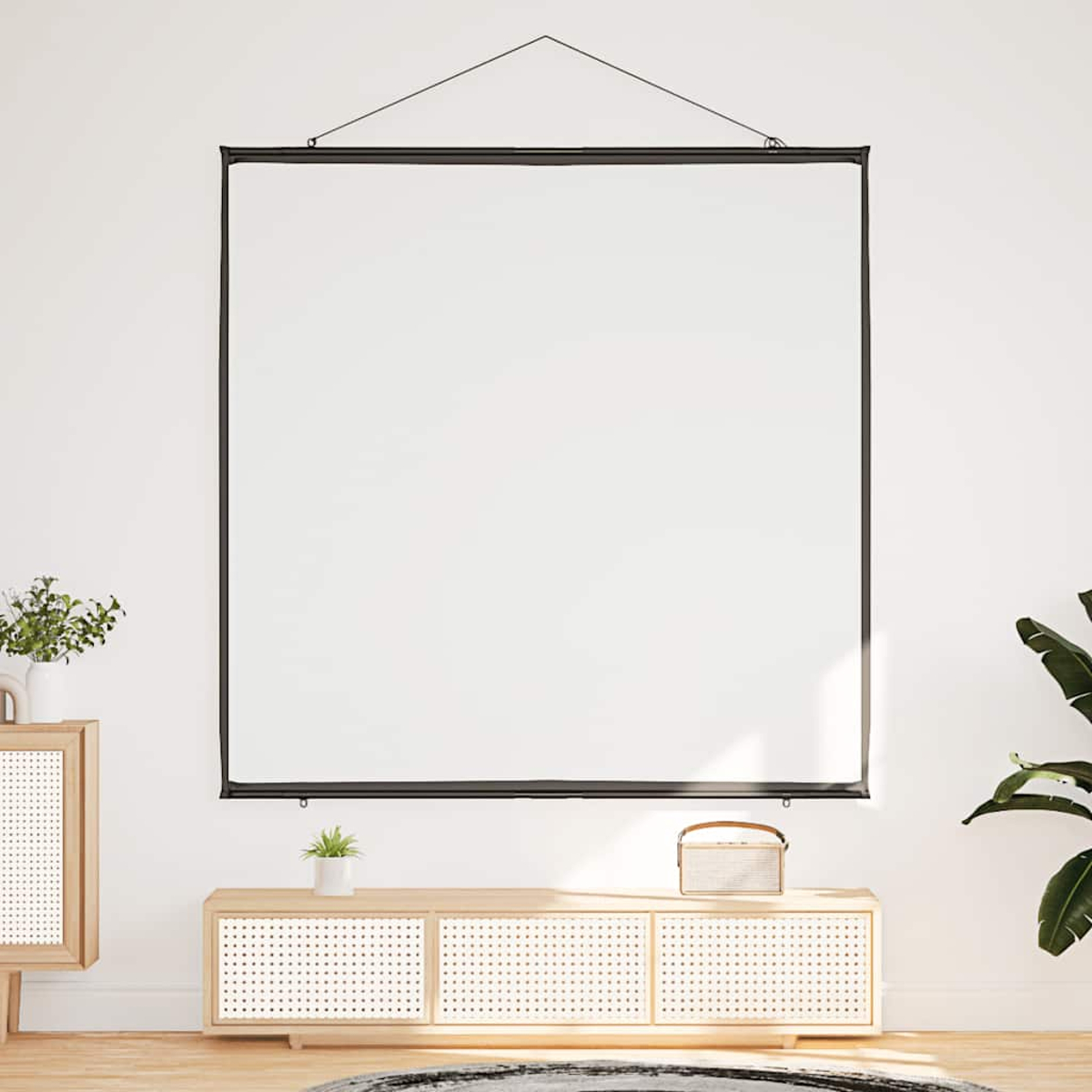 Eine weiße Projektionsleinwand hängt an einer weißen Wand. Darunter ein Holzschrank mit Pflanze, Lautsprecher und Grün. Es gibt auch eine Pflanze.