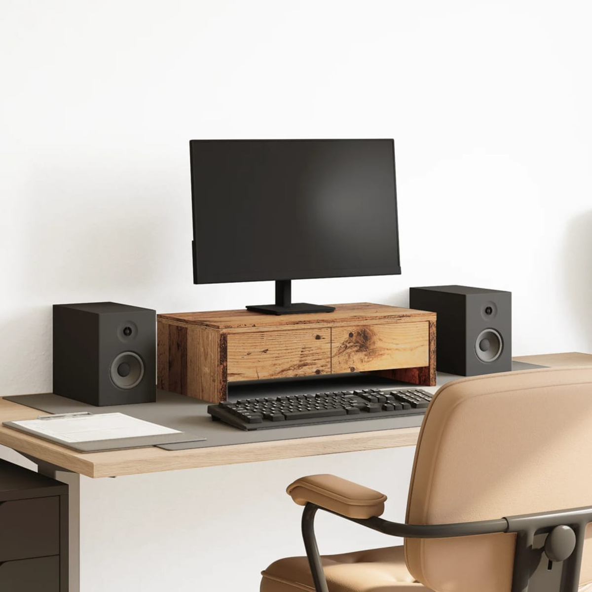 Ein Computer-Setup mit Monitor, Lautsprechern, Tastatur und Schreibtisch. Ein beiger Stuhl im Vordergrund und eine weiße Wand im Hintergrund.