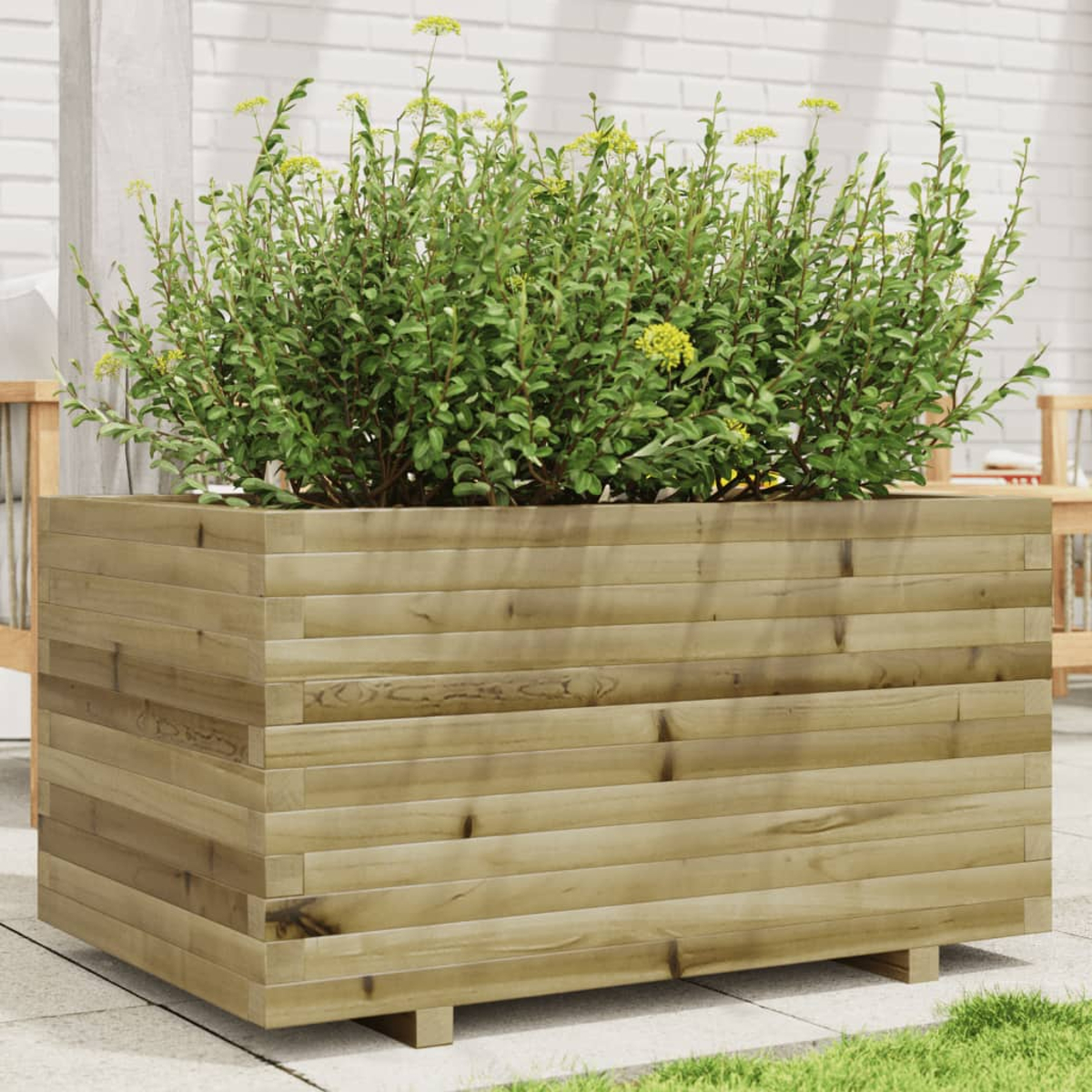 Ein großer hölzerner Pflanzkasten mit grünen Pflanzen und gelben Blüten steht auf einer Terrasse. Im Hintergrund befindet sich eine weiße Ziegelmauer.