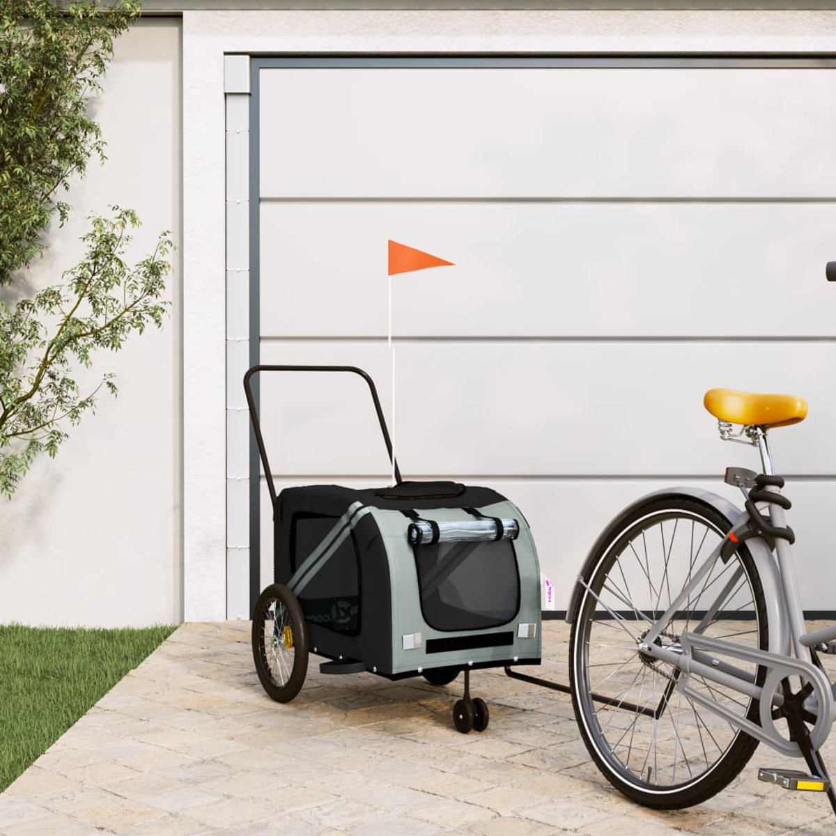 Ein Fahrrad mit gelbem Sattel ist mit einem Haustieranhänger mit orangefarbener Flagge verbunden. Im Hintergrund ist ein Garagentor.