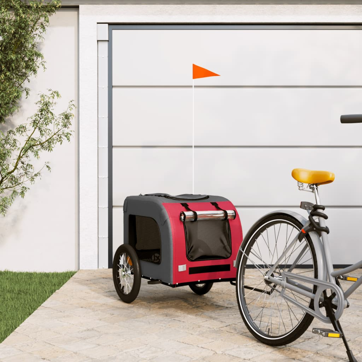Ein Fahrrad mit einem Tieranhänger parkt vor einer Garage. Am Anhänger ist eine orangefarbene Fahne. Daneben befinden sich grünes Gras und ein Baum.