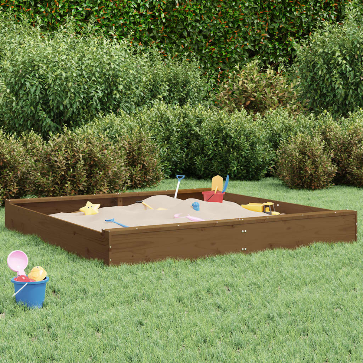 Ein Sandkasten mit Spielzeug auf grünem Gras. Büsche bilden den Hintergrund. Ein Eimer und eine Schaufel sind im Vordergrund.