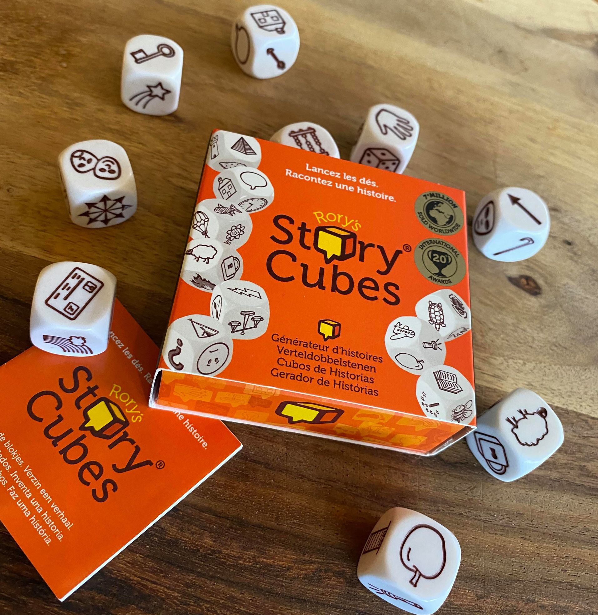 Eine orangefarbene Schachtel mit Rory's Story Cubes und Würfeln auf einer Holzoberfläche.