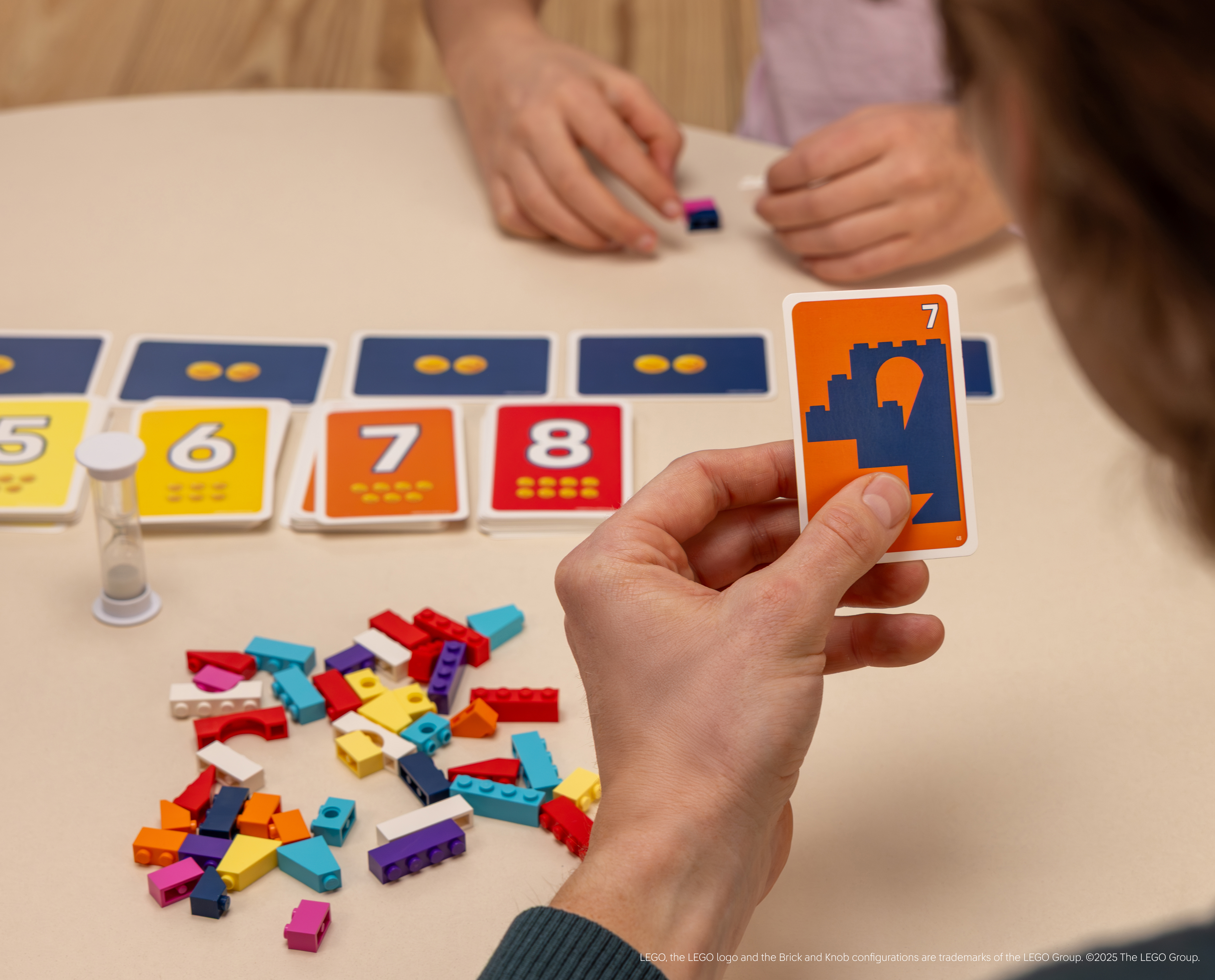Een persoon houdt een kaart met een kasteel vast. Andere kaarten en Lego-stenen liggen op tafel.