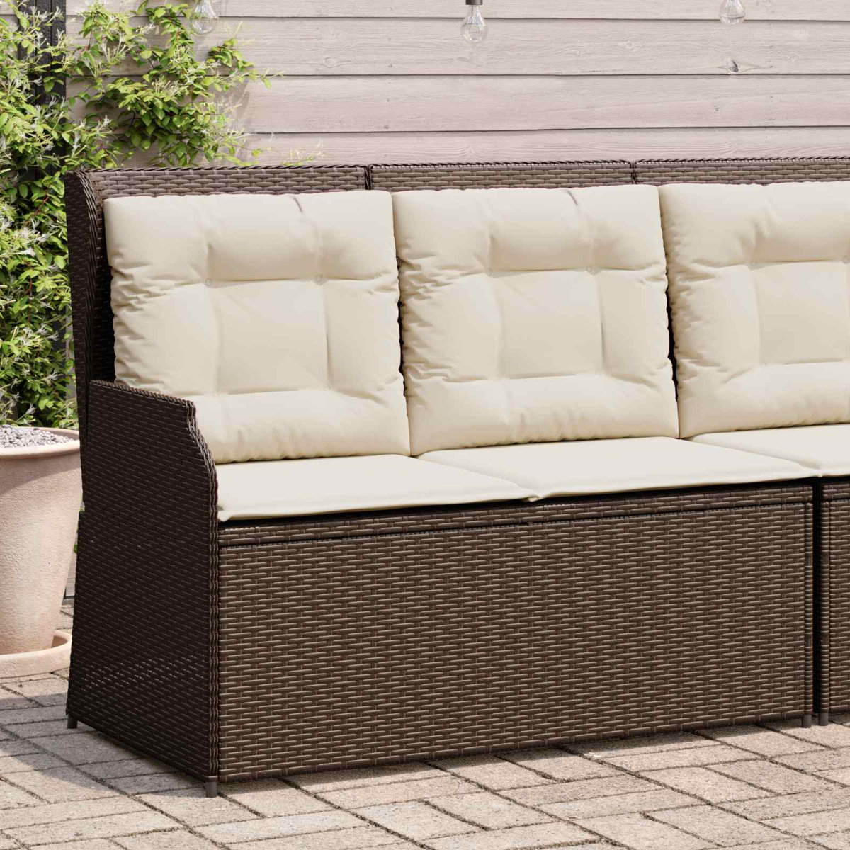 Braunes Korbmöbelsofa mit cremefarbenen Kissen. Im Hintergrund Holzpaneele und Pflanzen.